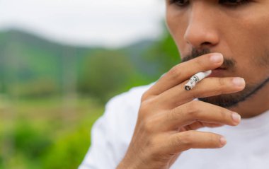 Genç adam açık havada sigara içiyor.