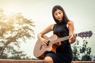 Mutlu kadın doğa arka plan ile gitar çalar.