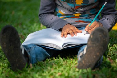 Parkta bir deftere yazan küçük çocuk.