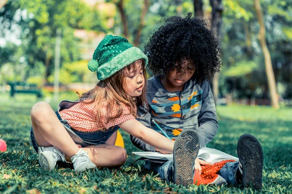 Escola menino e menina leitura livro juntos no parque . — Fotografia de Stock
