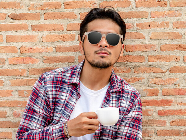 Young man holding coffee cup against brick wall.