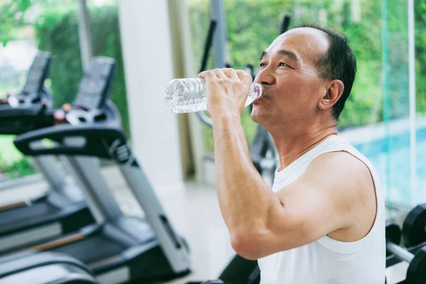 Senior man drink mineraalwater in het fitnesscentrum. — Stockfoto