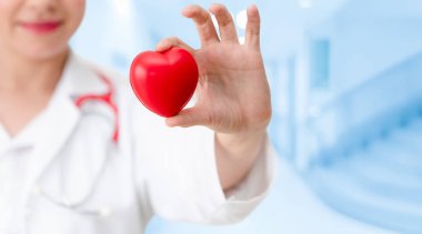 Hastane ofisinde kırmızı kalp tutan doktor.