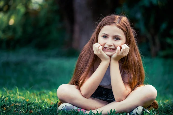 Glückliches süßes kleines Mädchen sitzt im Park. — Stockfoto