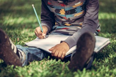 Parkta bir deftere yazan küçük çocuk.