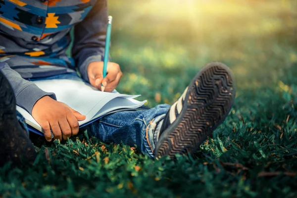 Parkta bir deftere yazan küçük çocuk.