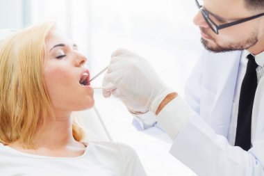 Diş kliniğinde hastayı muayene eden genç diş hekimi.