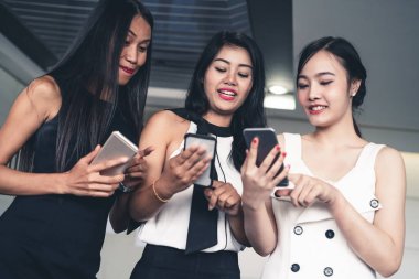 Üç kadın arkadaş cep telefonu aygıtıyla konuşuyor.