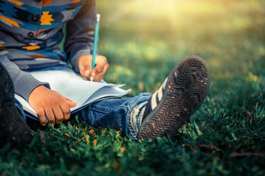 Parkta bir deftere yazan küçük çocuk.