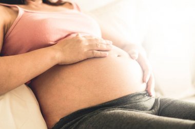 Hamile kadın evde çocuğuna bakarken mutlu hissediyor. Hamile karnında bebek tutan genç anne bekliyor. Doğum öncesi bakım ve kadın gebelik kavramı.