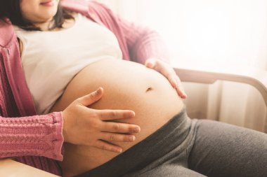 Hamile kadın evde çocuğuna bakarken mutlu hissediyor. Hamile karnında bebek tutan genç anne bekliyor. Doğum öncesi bakım ve kadın gebelik kavramı.