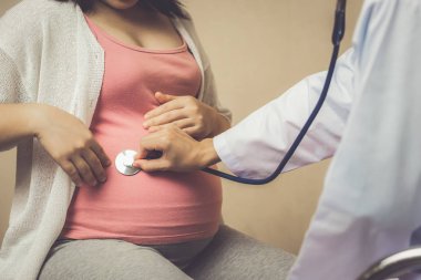 Mutlu hamile kadın gebelik konsültasyonu için hastane veya tıp kliniğinde jinekolog doktor ziyaret. Doktor bebek ve anne sağlık kontrolü için stetoskop ile hamile göbek muayene. Jinekoloji kavramı.