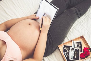 Hamile kadın evde çocuğuna bakarken mutlu hissediyor. Hamilelik notları yapan genç anne bekliyor. Doğum öncesi bakım ve kadın gebelik kavramı.