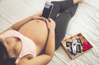 Hamile kadın evde çocuğuna bakarken mutlu hissediyor. Genç anne bekleyen fotoğraf tutuyor. Doğum öncesi bakım ve kadın gebelik kavramı.