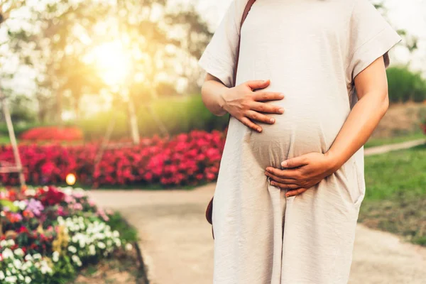 妊娠中の女性は 子供の世話をしながら庭で幸せを感じています 妊娠中の腹に赤ちゃんを抱いている若い期待の母親 出産前ケアと女性妊娠概念 — ストック写真