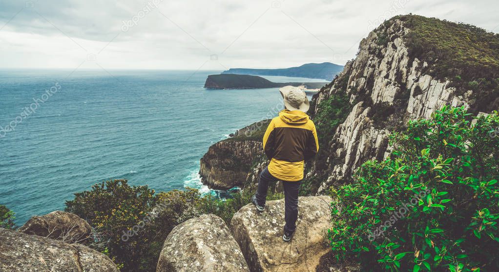 Young man trekker hiking on coast cliff of Tasman National Park in Tasman peninsula, Three Capes Track near Port Arthur in Tasmania, Australia.
