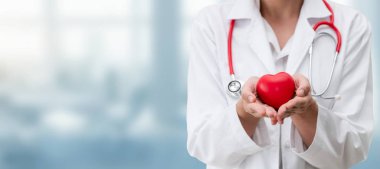 Hastane ofisinde kırmızı kalp tutan doktor.