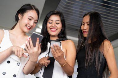 Üç kadın arkadaş cep telefonu aygıtıyla konuşuyor.