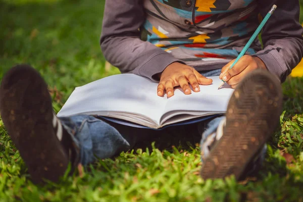 Niño pequeño escribiendo en un cuaderno en el parque . —  Fotos de Stock