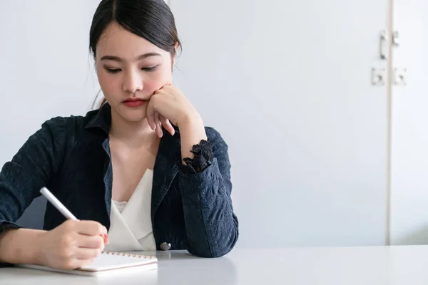 Beautiful young Asian woman writes on notebook.