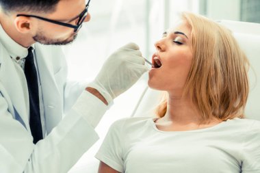 Diş kliniğinde hastayı muayene eden genç diş hekimi.