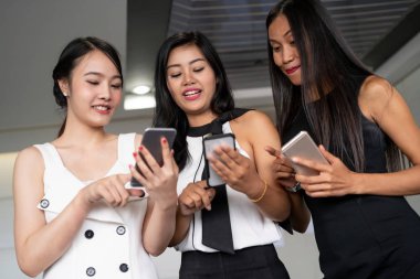 Üç kadın arkadaş cep telefonu aygıtıyla konuşuyor.
