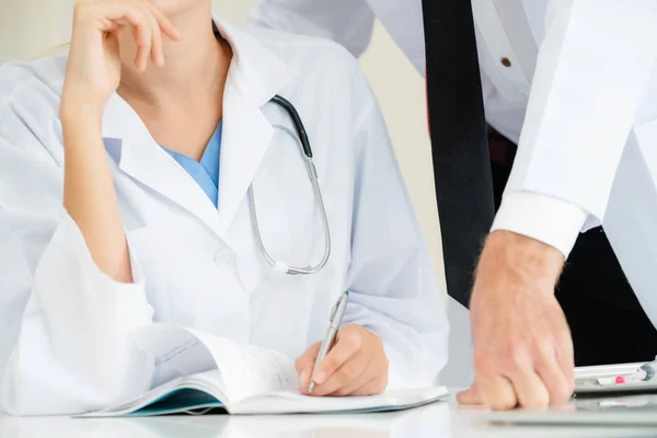 Doctor escribe informe en el escritorio con otro médico . — Foto de Stock