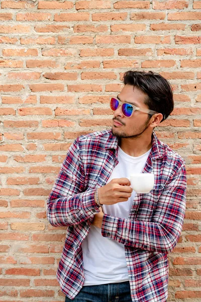 Joven sosteniendo taza de café contra la pared de ladrillo . — Foto de Stock