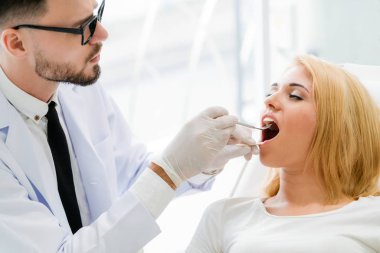 Diş kliniğinde hastayı muayene eden genç diş hekimi.