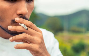 Genç adam açık havada sigara içiyor.