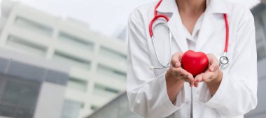 Hastane ofisinde kırmızı kalp tutan doktor.
