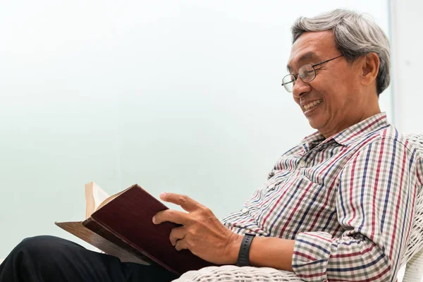 Senior asiatischer Mann liest Buch auf Stuhl zu Hause. — Stockfoto