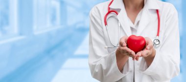 Hastane ofisinde kırmızı kalp tutan doktor.