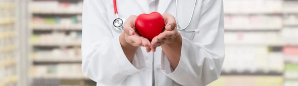 Doctor sosteniendo un corazón rojo en la oficina del hospital . — Foto de Stock