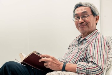 Evde sandalyede kitap okuyan Kıdemli Asyalı adam.