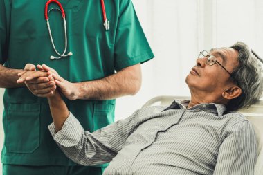 Erkek doktor kıdemli yetişkin hastanın elini tutarak.