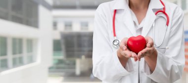 Hastane ofisinde kırmızı kalp tutan doktor.