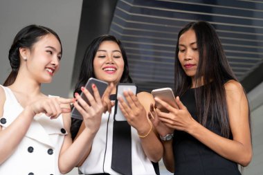 Üç kadın arkadaş cep telefonu aygıtıyla konuşuyor.