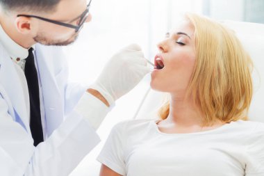 Diş kliniğinde hastayı muayene eden genç diş hekimi.