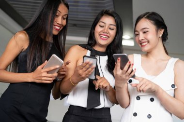 Üç kadın arkadaş cep telefonu aygıtıyla konuşuyor.