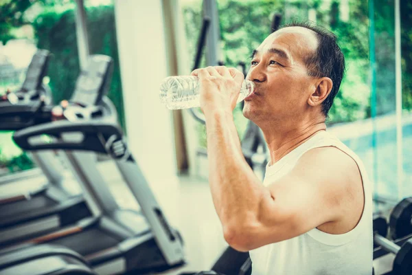 Uomo anziano bere acqua minerale nel centro fitness . — Foto Stock