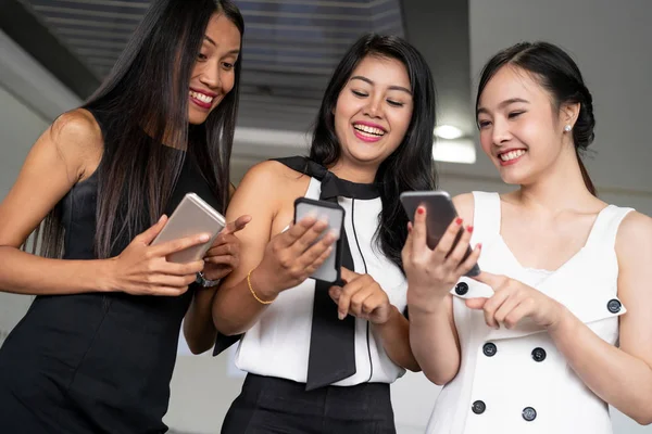Three women friends chat with mobile phone device.