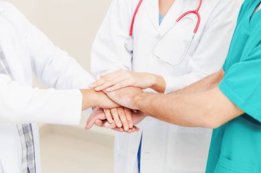 Doktor, cerrah ve hemşire el ele tutuşuyor.