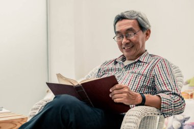 Evde sandalyede kitap okuyan Kıdemli Asyalı adam.