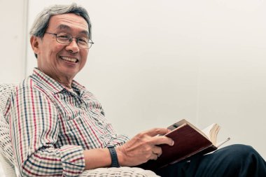 Evde sandalyede kitap okuyan Kıdemli Asyalı adam.