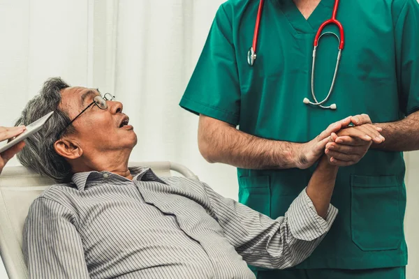 Male doctor holding hand of senior adult patient.