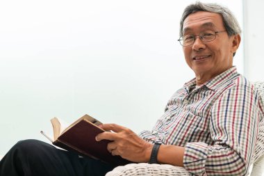 Evde sandalyede kitap okuyan Kıdemli Asyalı adam.