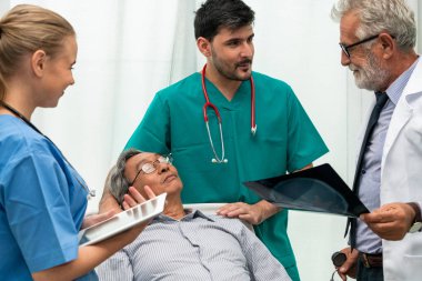 Doktor ekibi, hastane koğuş odasında yatakta yatan kıdemli yetişkin hastanın x ışını görüntüsü ile çalışır. Tıbbi grup ekip çalışması ve sağlık kişi personel hizmeti.