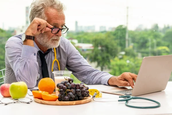 Dizüstü bilgisayar üzerinde çalışan kıdemli erkek beslenme uzmanı doktor. — Stok fotoğraf