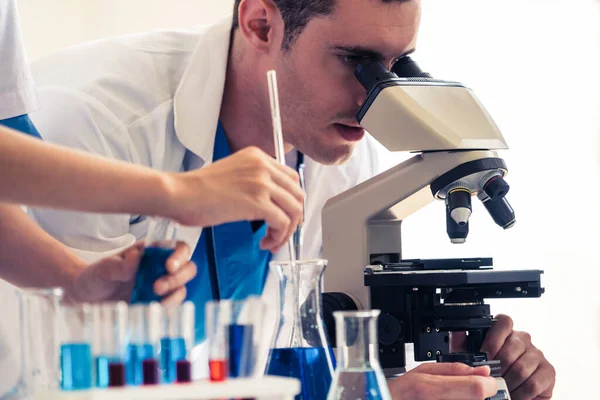 학자들은 시험관 장비로 생화학 표본을 조사하면서 실험실에서 작업하는 실험실 코트를 — 스톡 사진